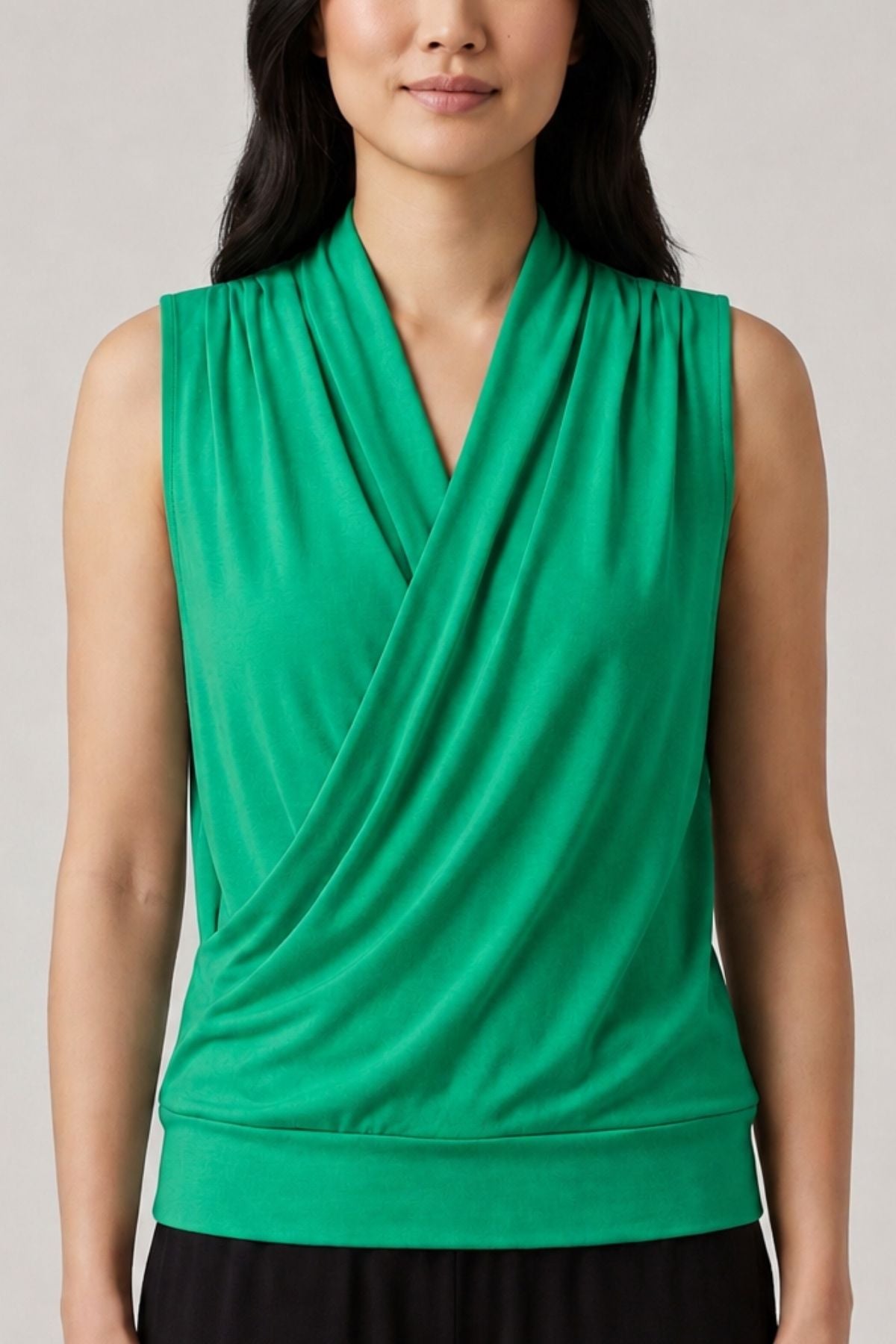A woman wearing a bright green sleeveless wrap-style top with a draped cowl neckline, shown from the shoulders to the waist against a plain light gray studio background.