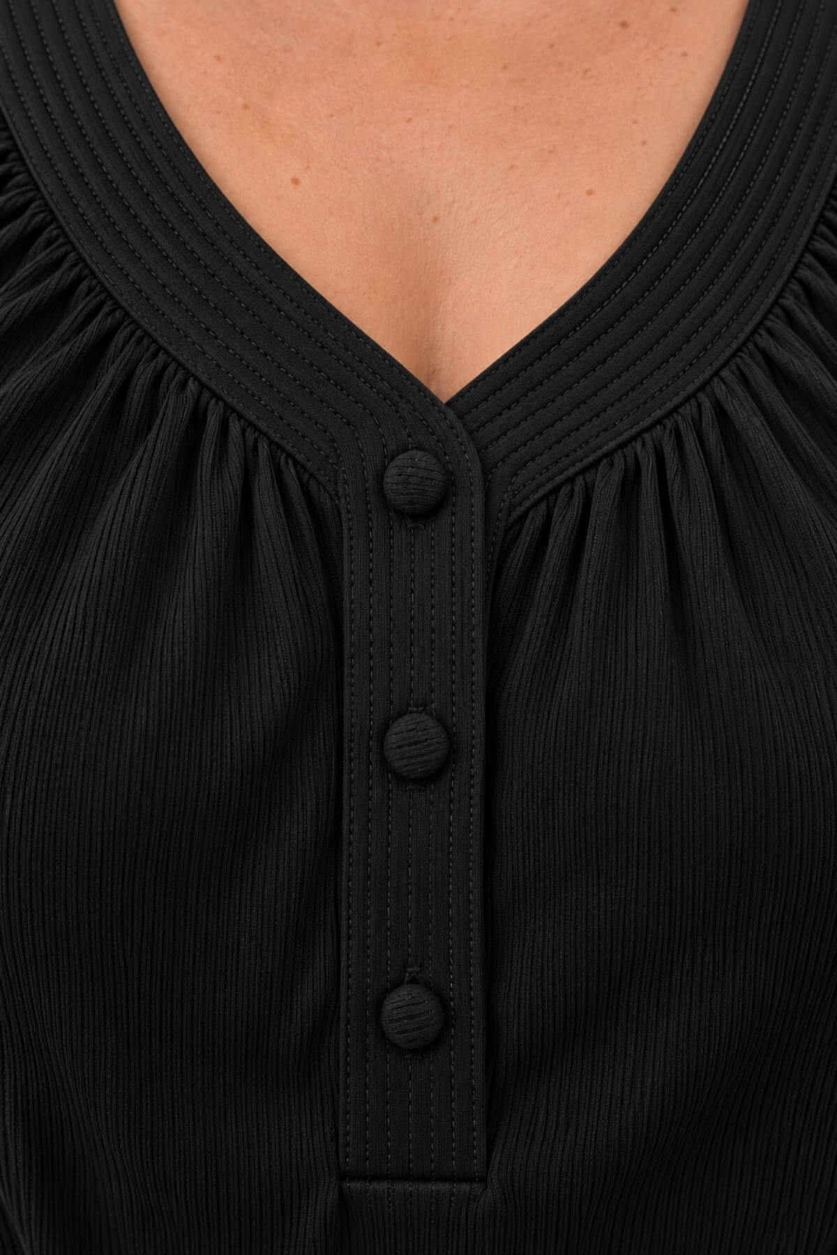 Close-up of a black ribbed top with a V-neckline, gathered neckline, and three dark buttons down the center front.