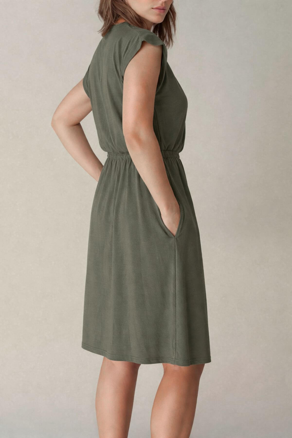 Back view of a woman wearing a green nursing dress against a plain background