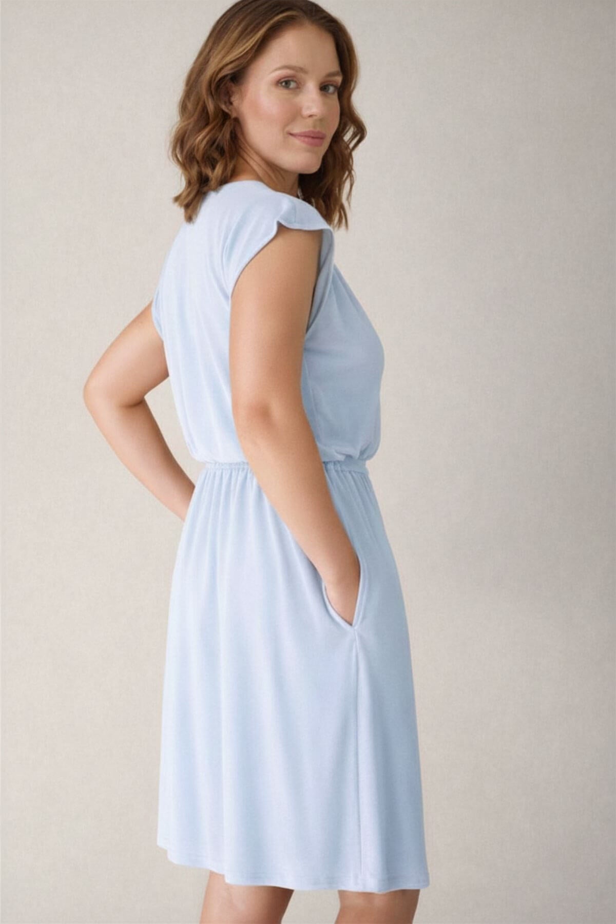 Woman wearing a light blue nursing dress against a plain background back view