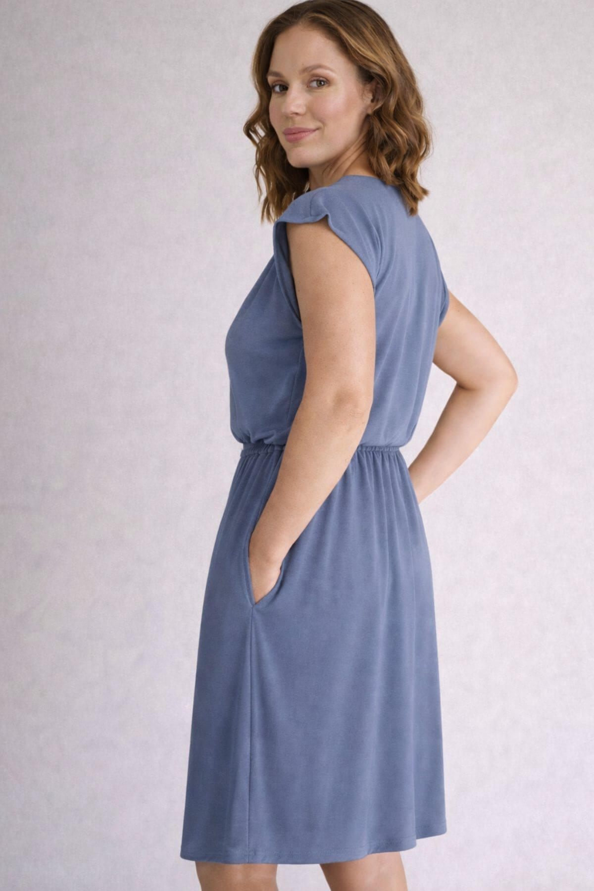 Back view of a woman wearing a gray blue nursing dress against a light gray background