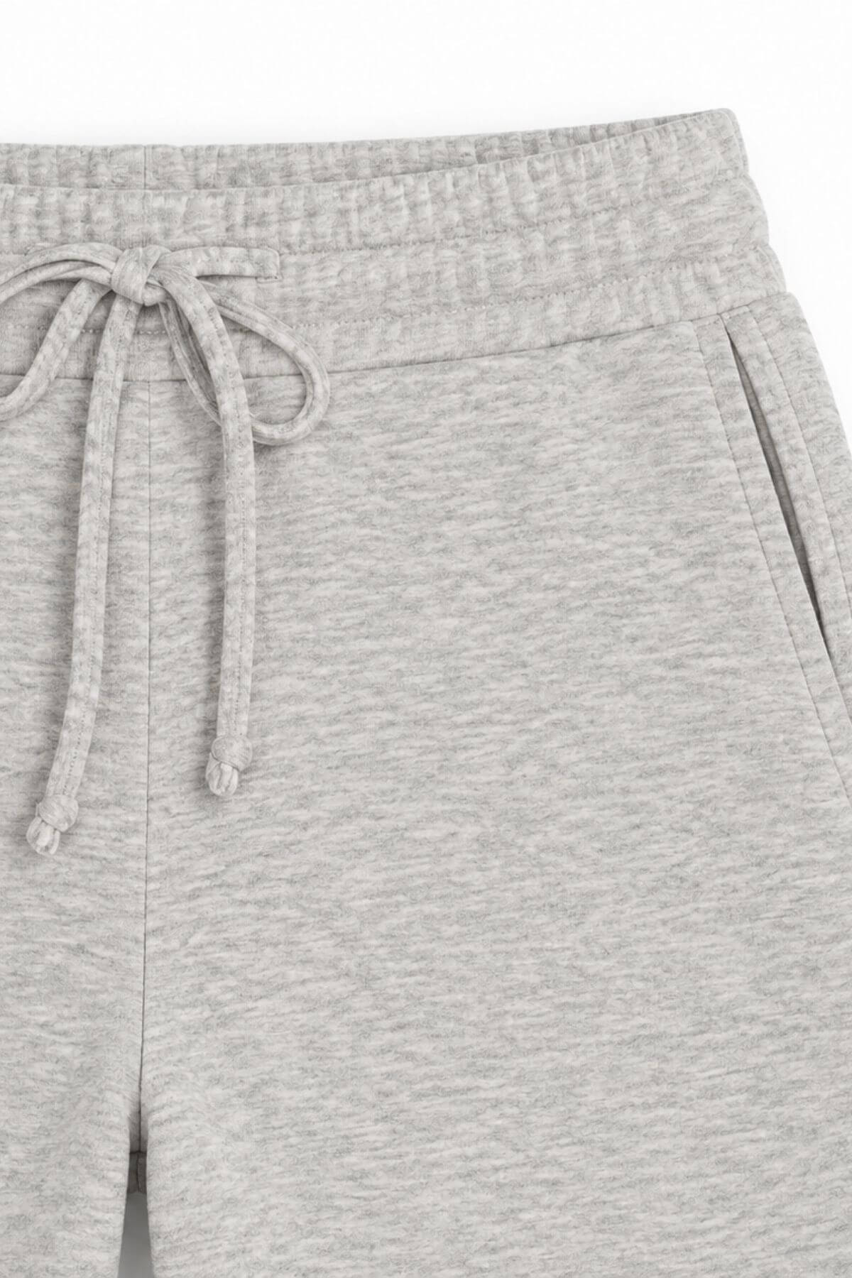 Close-up of light heather gray sweatpants showing the elastic waistband, drawstring, and side pocket.