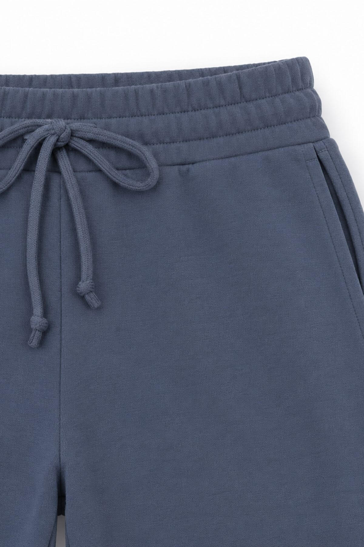 Close-up of a pair of slate blue sweatpants showing the elastic waistband, drawstring, and side pocket.