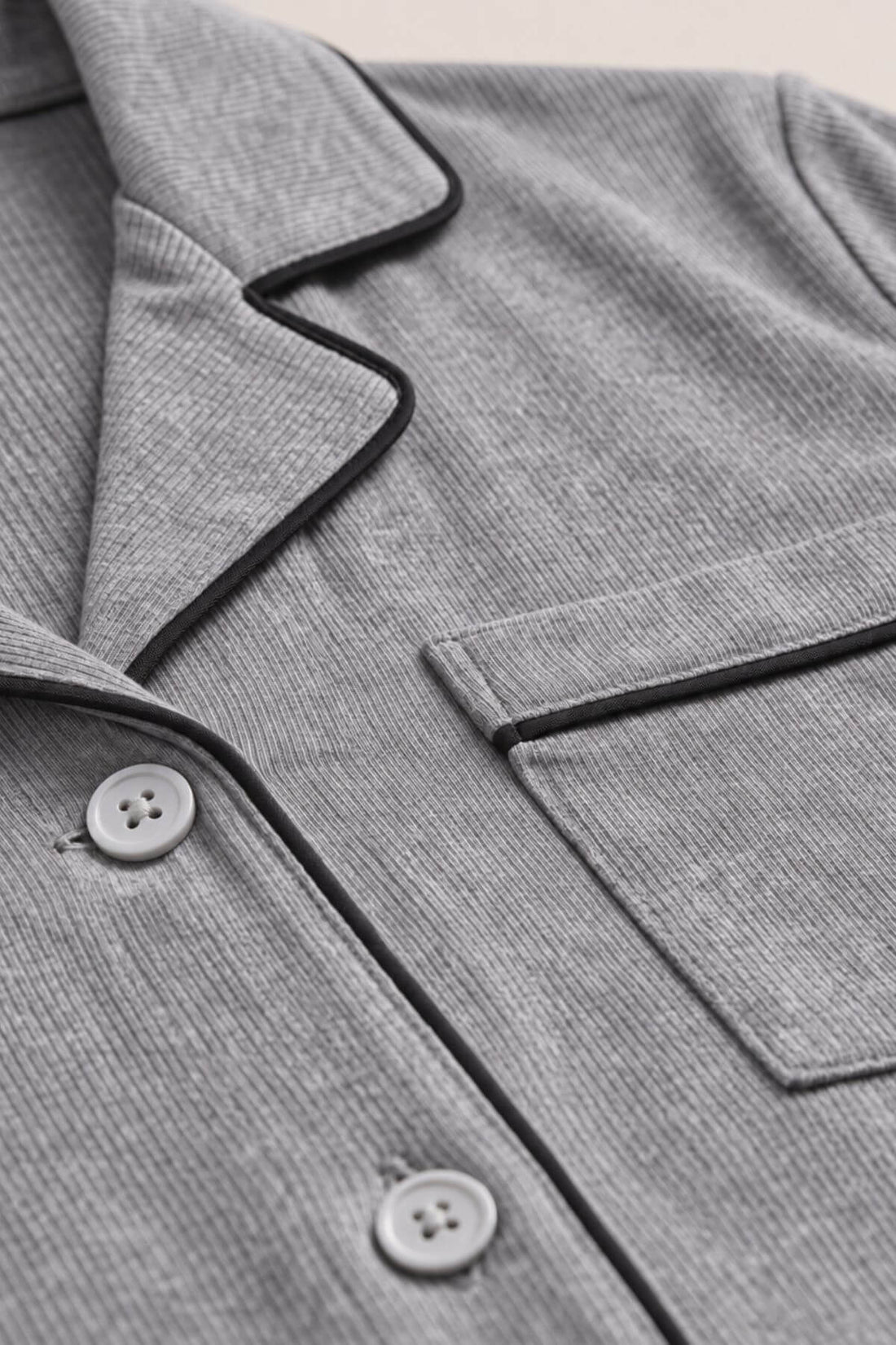 Close-up of a gray ribbed pajama top showing the collar, button placket, chest pocket, and black piping trim.