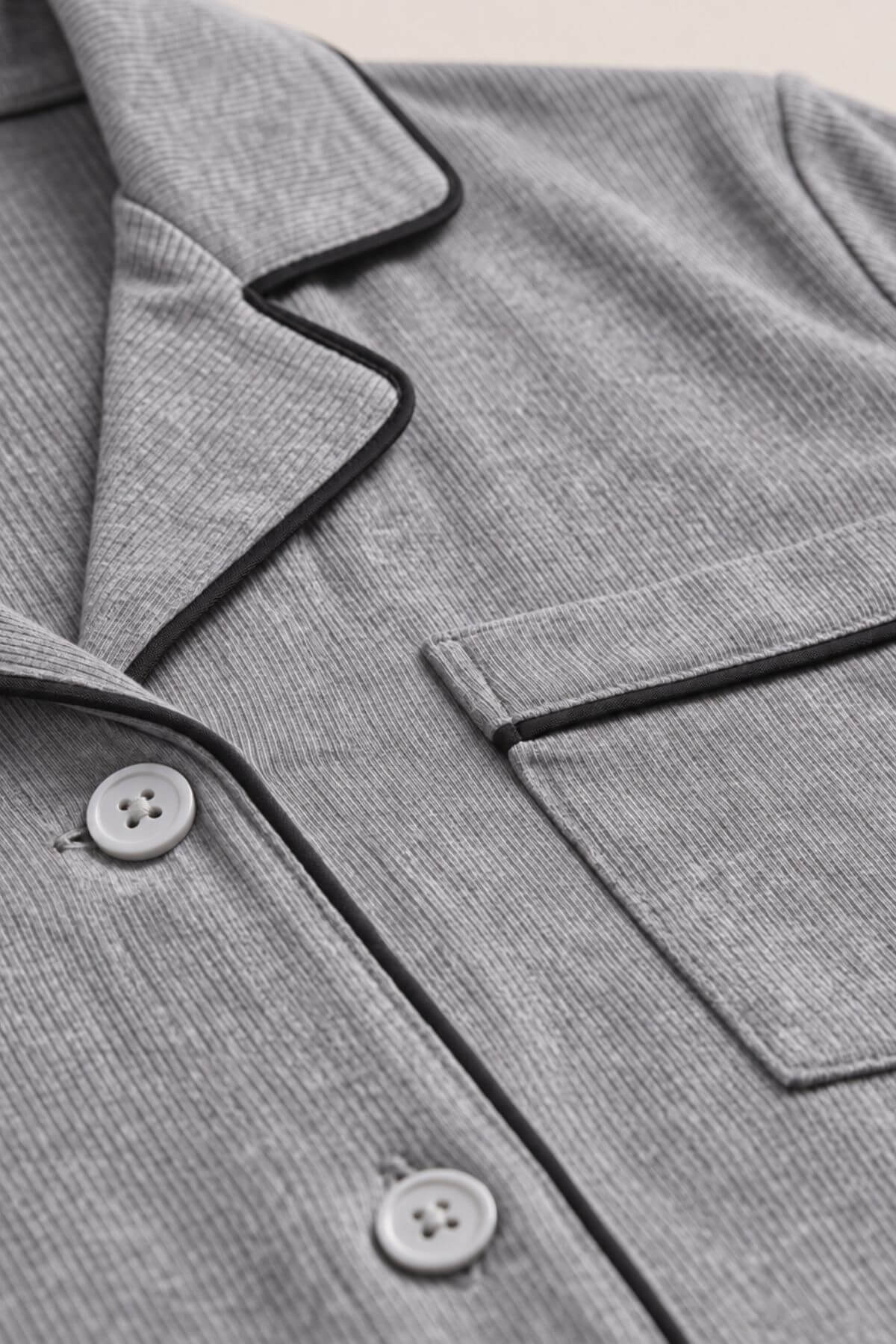 Close-up of a gray ribbed pajama top showing the collar, button placket, chest pocket, and black piping trim.