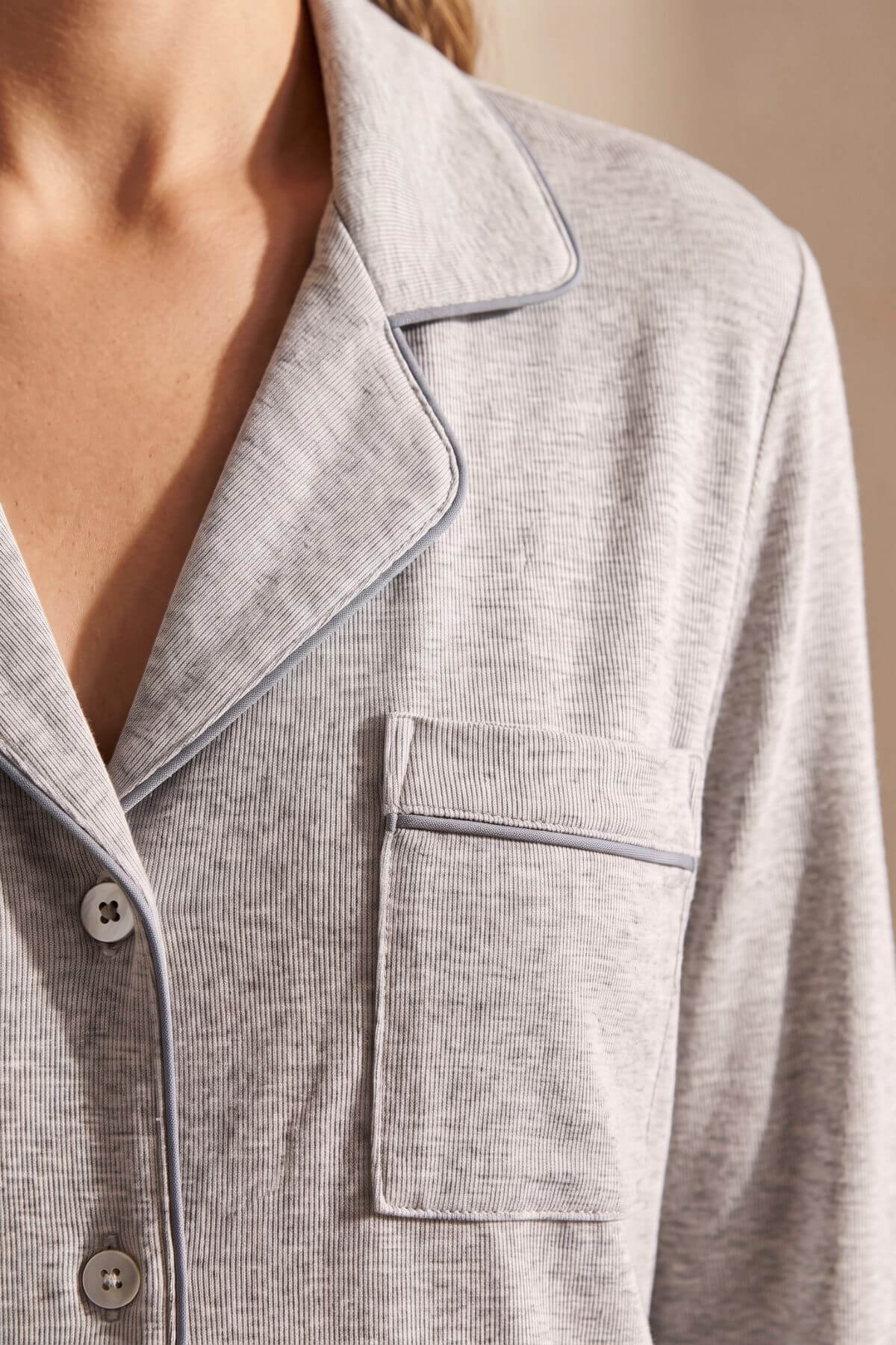 Close-up of a person wearing a light gray ribbed pajama top with contrasting dark piping, showing the collar, chest pocket, and buttons.