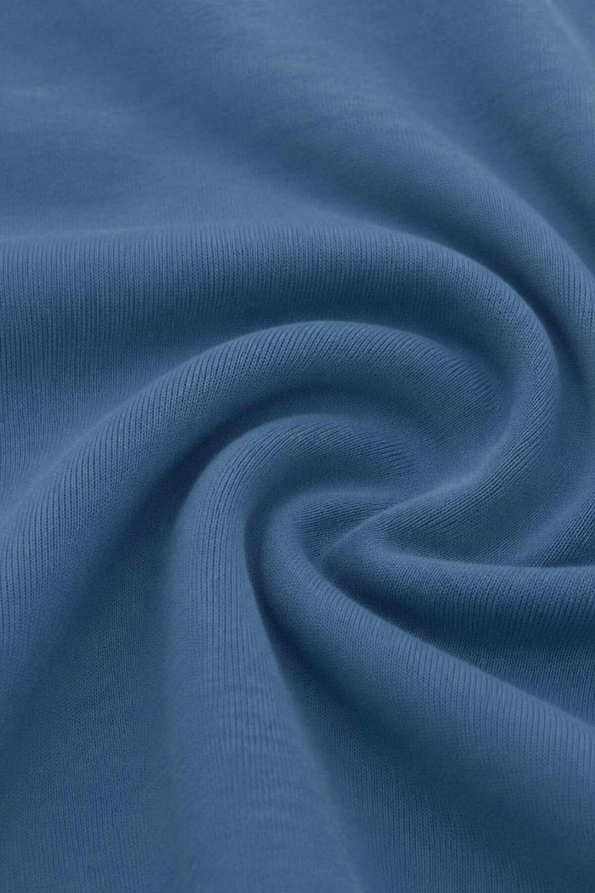 A close-up of draped blue fabric with a fine ribbed texture, arranged in a spiral pattern..