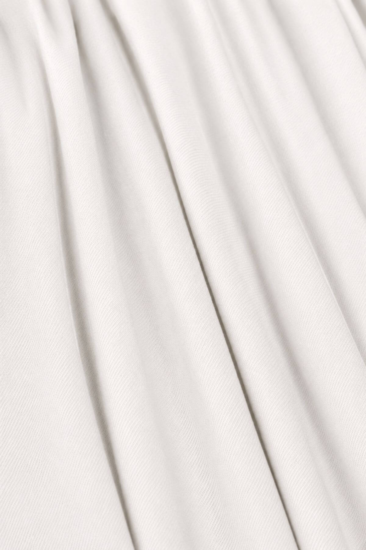 A close-up of draped off-white fabric with soft vertical folds and a fine woven texture.