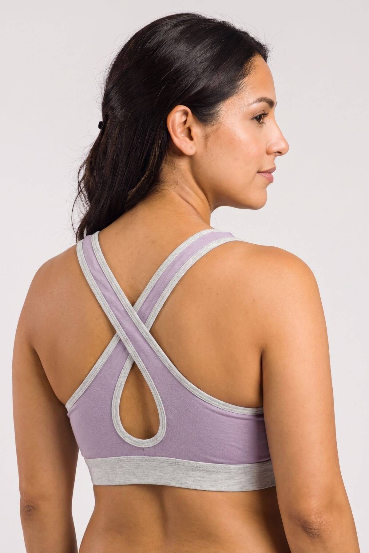 A woman shown from the back wearing a lavender and light gray sports bra with a crossover crisscross back design and a keyhole cutout.