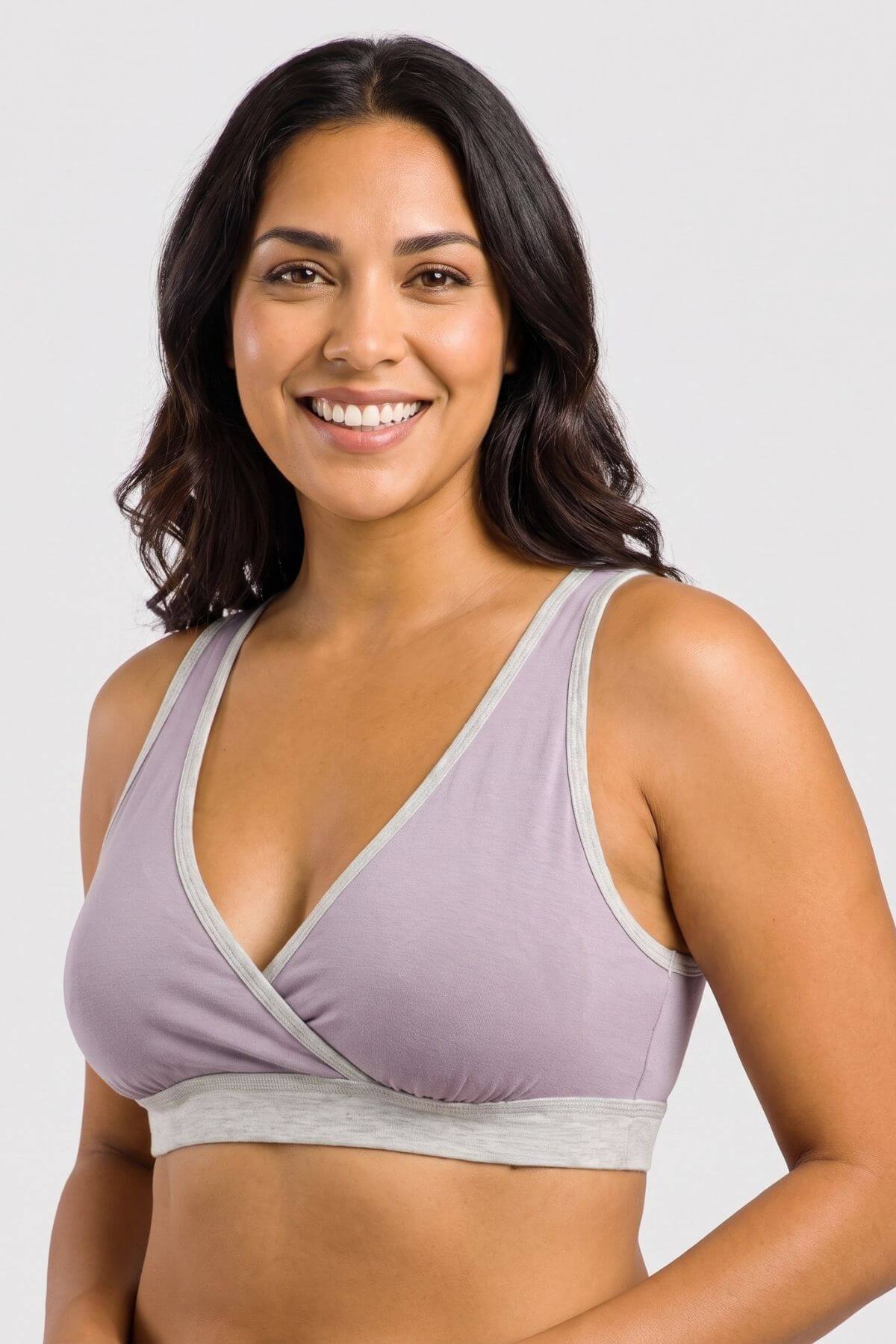 A smiling woman with dark hair wearing a light purple/lavender wrap-style bra with light gray trim and band, photographed against a plain light gray studio background.