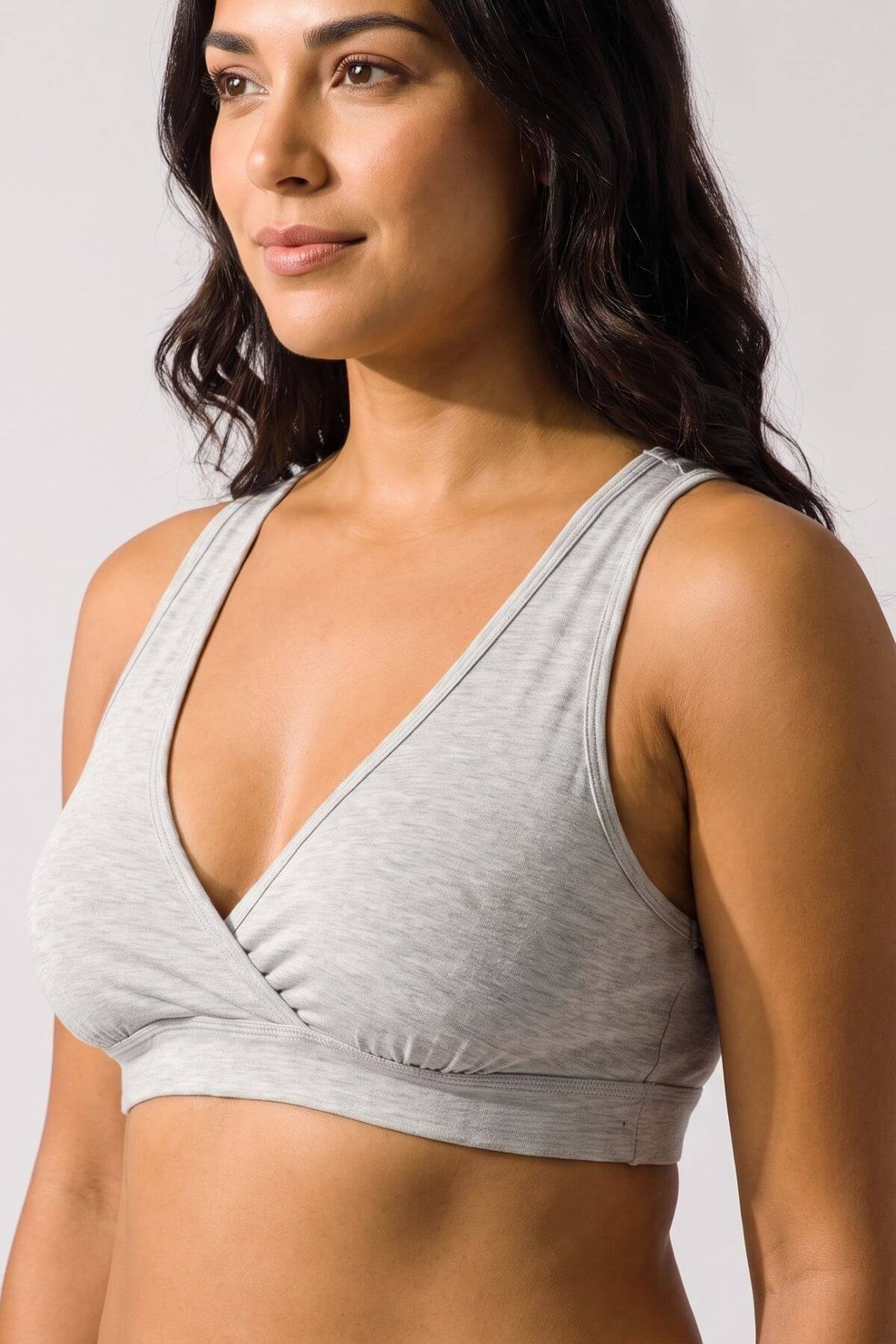 A woman wearing a light gray heathered wrap-style sports bra, shown from the chest up against a plain light gray studio background.