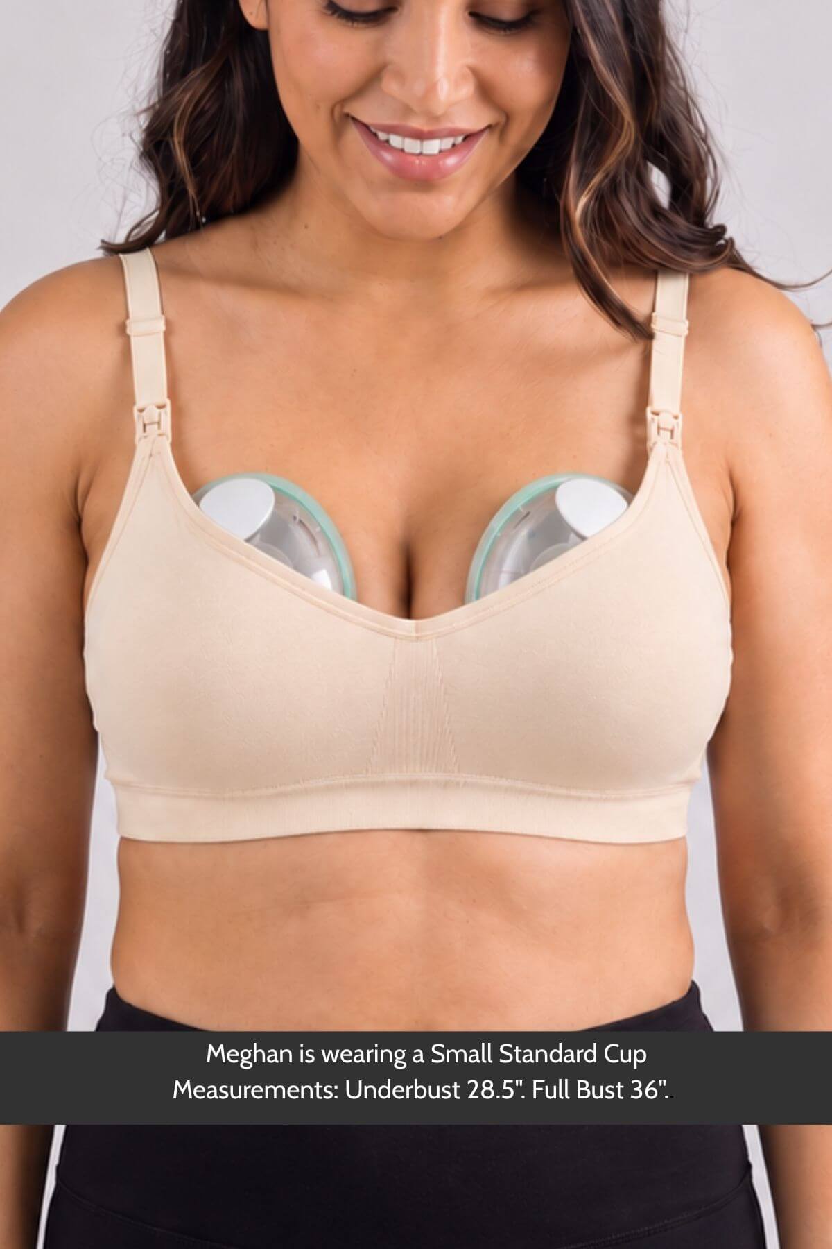 A woman wearing the Stages Maternity, Nursing, Wearable Pump & Everyday Bra in Sunkissed Rose with underwire cups, with two clear breast compression devices inserted into the cups. A text banner at the bottom provides sizing information for Meghan.