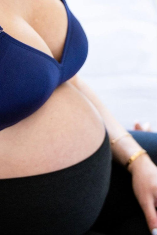 the supermom silhouette nursing and hands free pumping bra in indigo worn by a pregnant woman wearing black leggings.