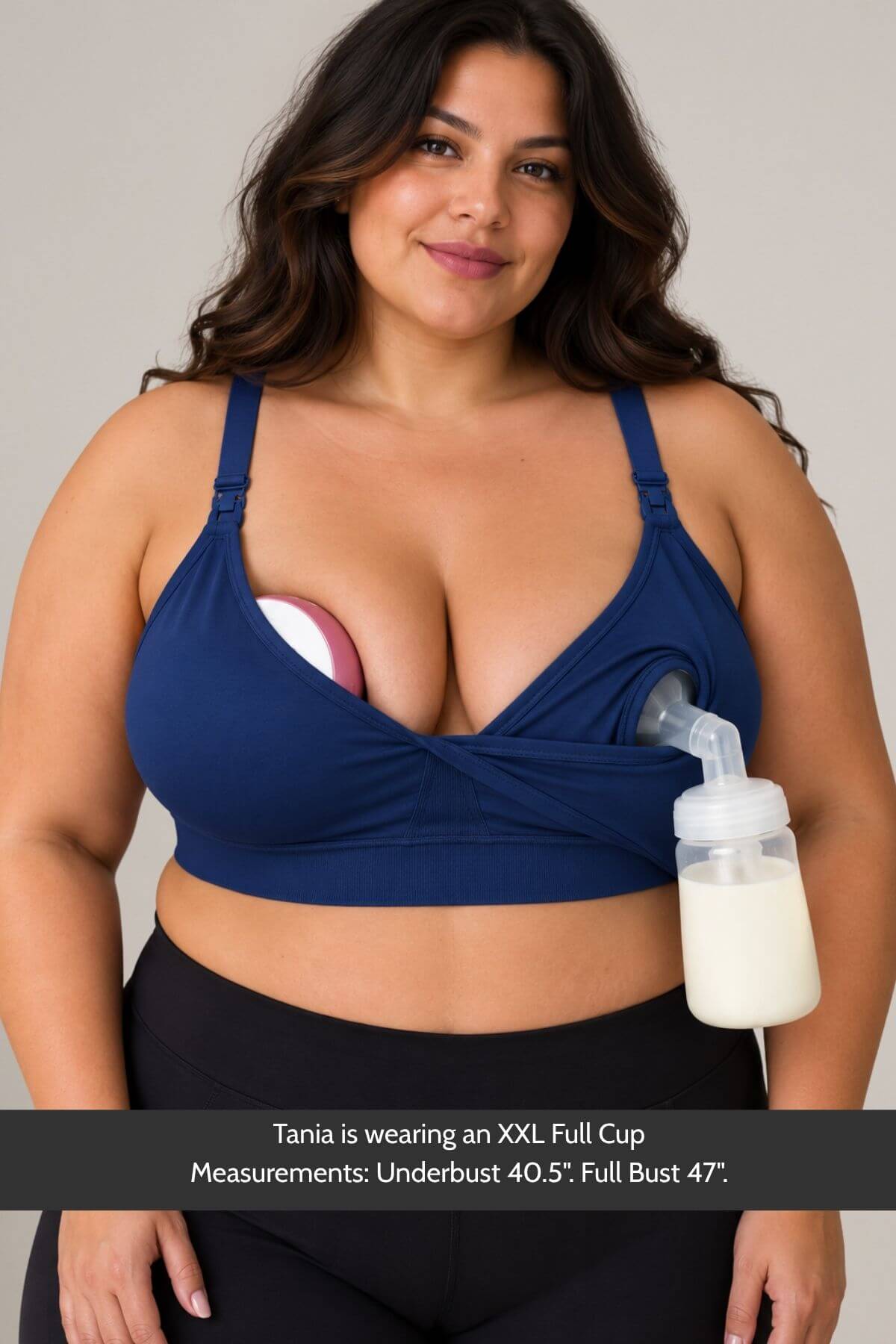 A plus size woman wearing the supermom silhouette nursing and hands free pumping bra in color indigo with a breast pump attached, shown against a plain light gray background. A text banner at the bottom provides cup size and measurement information.