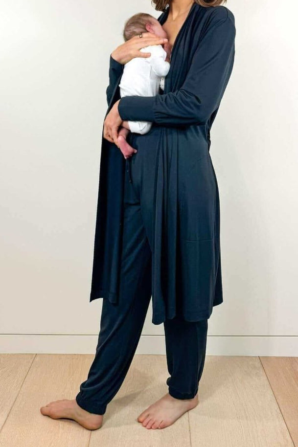 A woman wearing a light blue, long-sleeved jersey robe with pockets and a belt, holding a cup and a mobile phone.