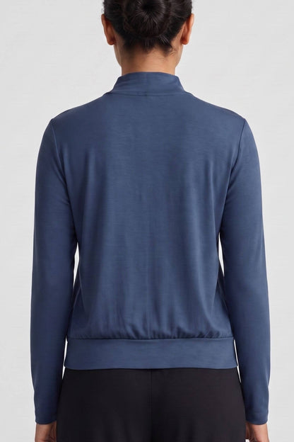 A person shown from the back wearing a long-sleeve blue mock-neck top and black pants against a light gray studio background.