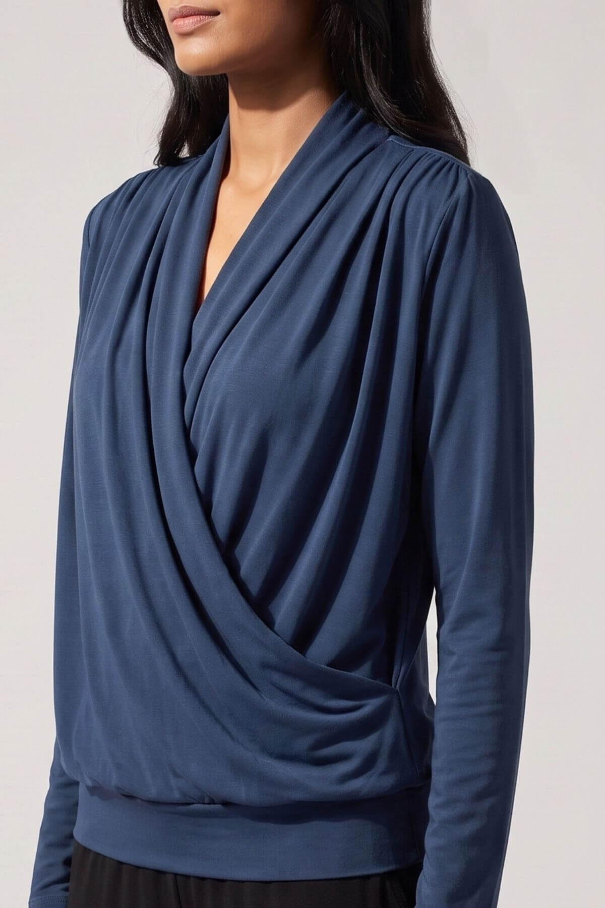 A woman wearing a navy blue long-sleeve draped wrap top, shown from the chin down against a plain light background.