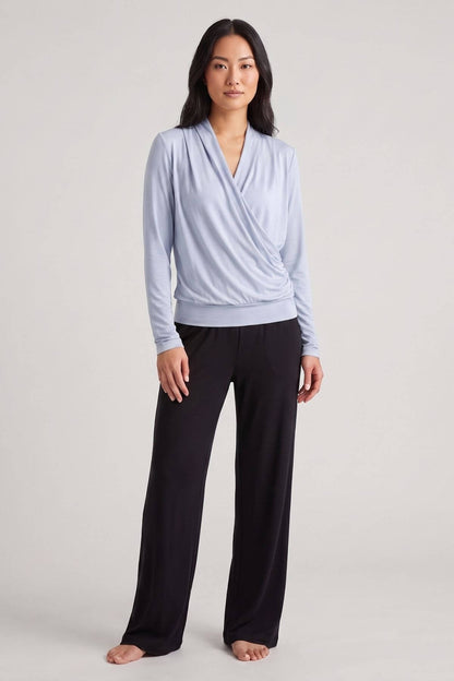 A woman modeling a light blue long-sleeve wrap top and black wide-leg pants against a neutral light gray studio background.