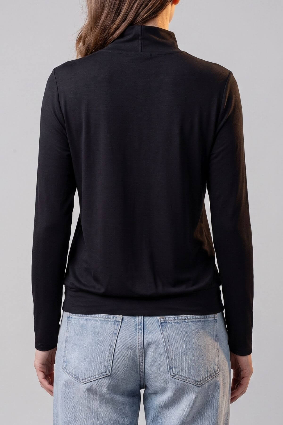 A woman shown from the back wearing a black long-sleeve mock neck top and light blue jeans against a plain light gray studio background.d.