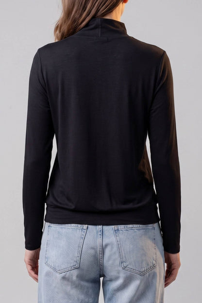 A woman shown from the back wearing a black long-sleeve mock neck top and light blue jeans against a plain light gray studio background.d.