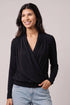 A woman wearing a black long-sleeve wrap-style top with a draped V-neck, paired with light blue jeans, photographed against a plain light gray studio background.