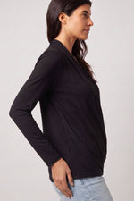 A woman wearing a black long-sleeve wrap-style top, shown in profile against a light gray studio background.d.#color_midnight