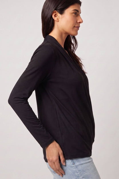 A woman wearing a black long-sleeve wrap-style top, shown in profile against a light gray studio background.d.