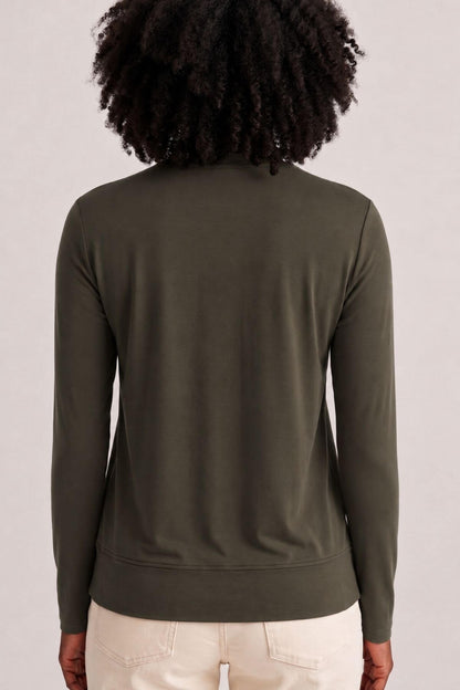 A person shown from the back wearing a dark olive green long-sleeve top and light beige pants against a plain light gray studio background.