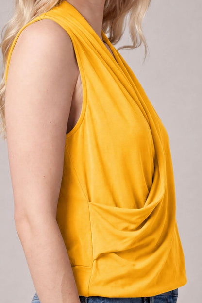 A close-up side view of a woman wearing a sleeveless draped top in a rich mustard yellow color, paired with blue jeans against a neutral gray background..