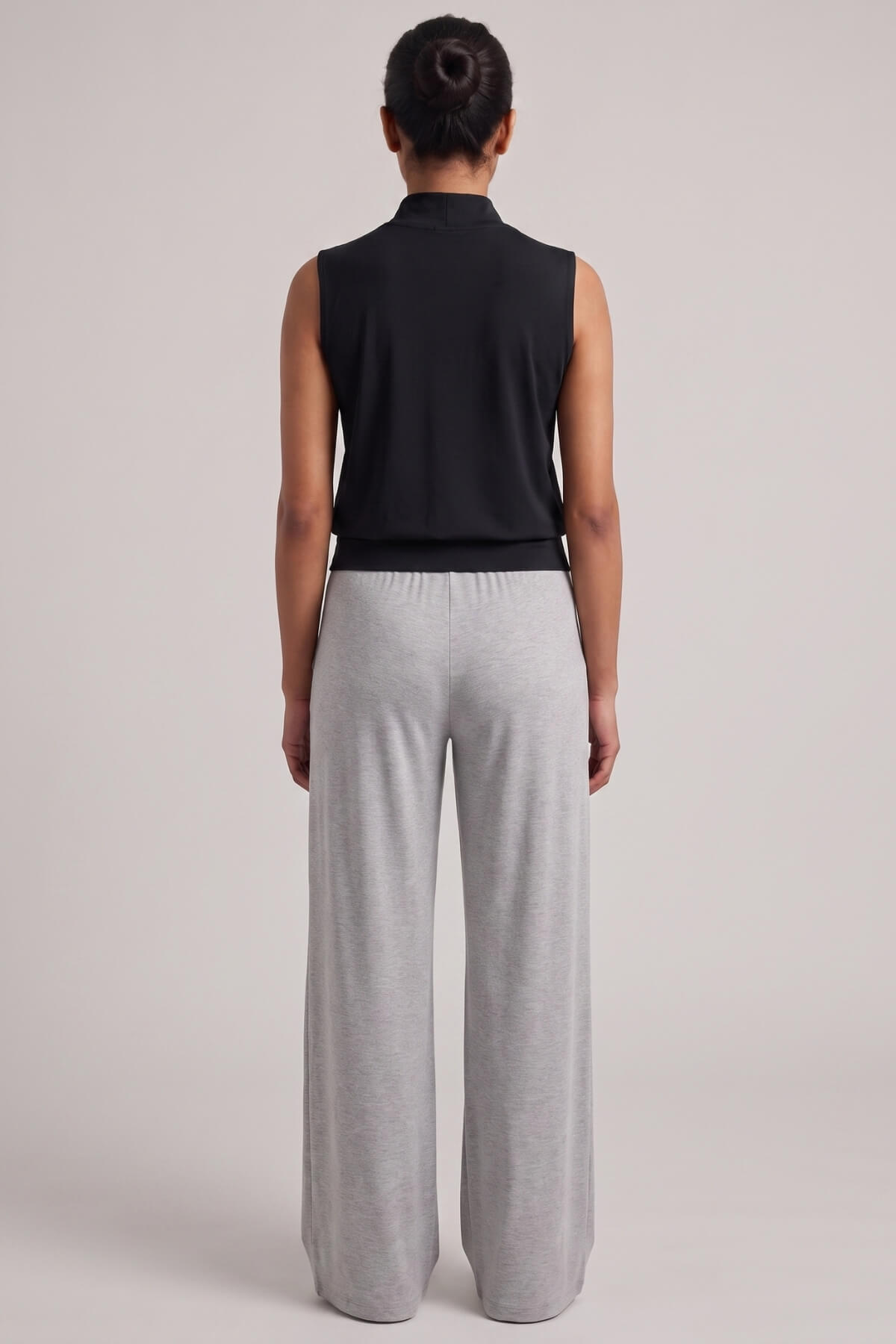 A model shown from the back wearing a black sleeveless mock-neck top and light gray wide-leg sweatpants against a solid light gray studio background.