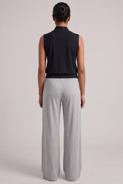 A model shown from the back wearing a black sleeveless mock-neck top and light gray wide-leg sweatpants against a solid light gray studio background.