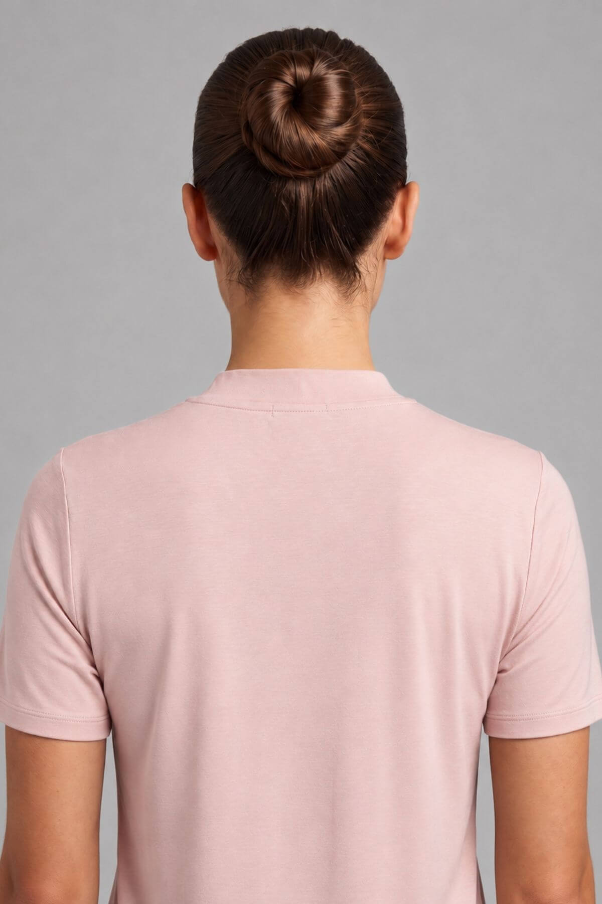 Back view of a person wearing a light pink short-sleeve crewneck t-shirt against a solid gray background.