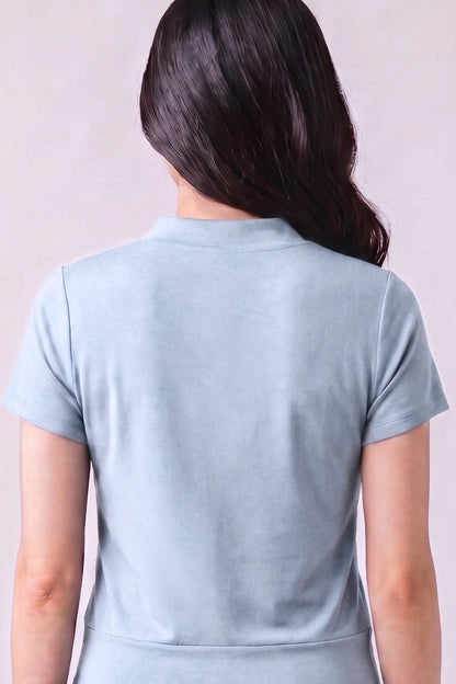 A woman viewed from the back wearing a light blue short-sleeve top against a plain light background.