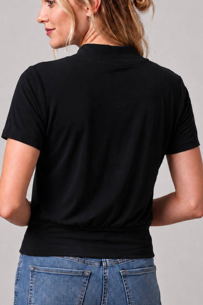 A woman shown from the back wearing a black short-sleeve mock neck top and blue jeans against a light gray studio background.
