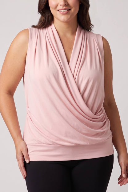 A woman wearing a sleeveless dusty pink draped wrap-style top with black leggings, shown against a light gray studio background.