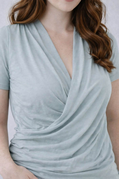 Woman wearing a light gray green blue nursing top with a draped neckline