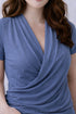 Woman wearing a light gray blue nursing top with a draped neckline on a light background