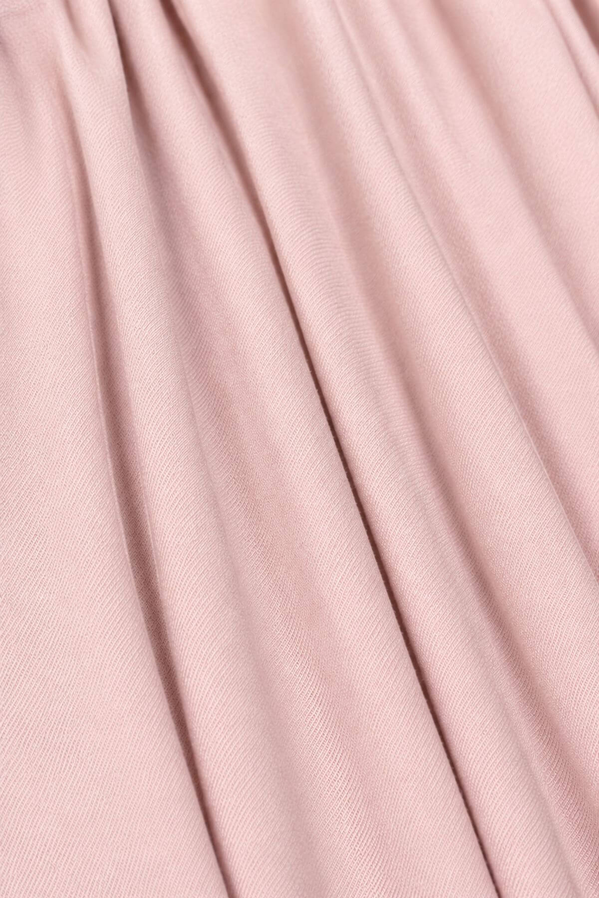 A close-up of draped dusty pink fabric with soft vertical folds and a fine woven texture.