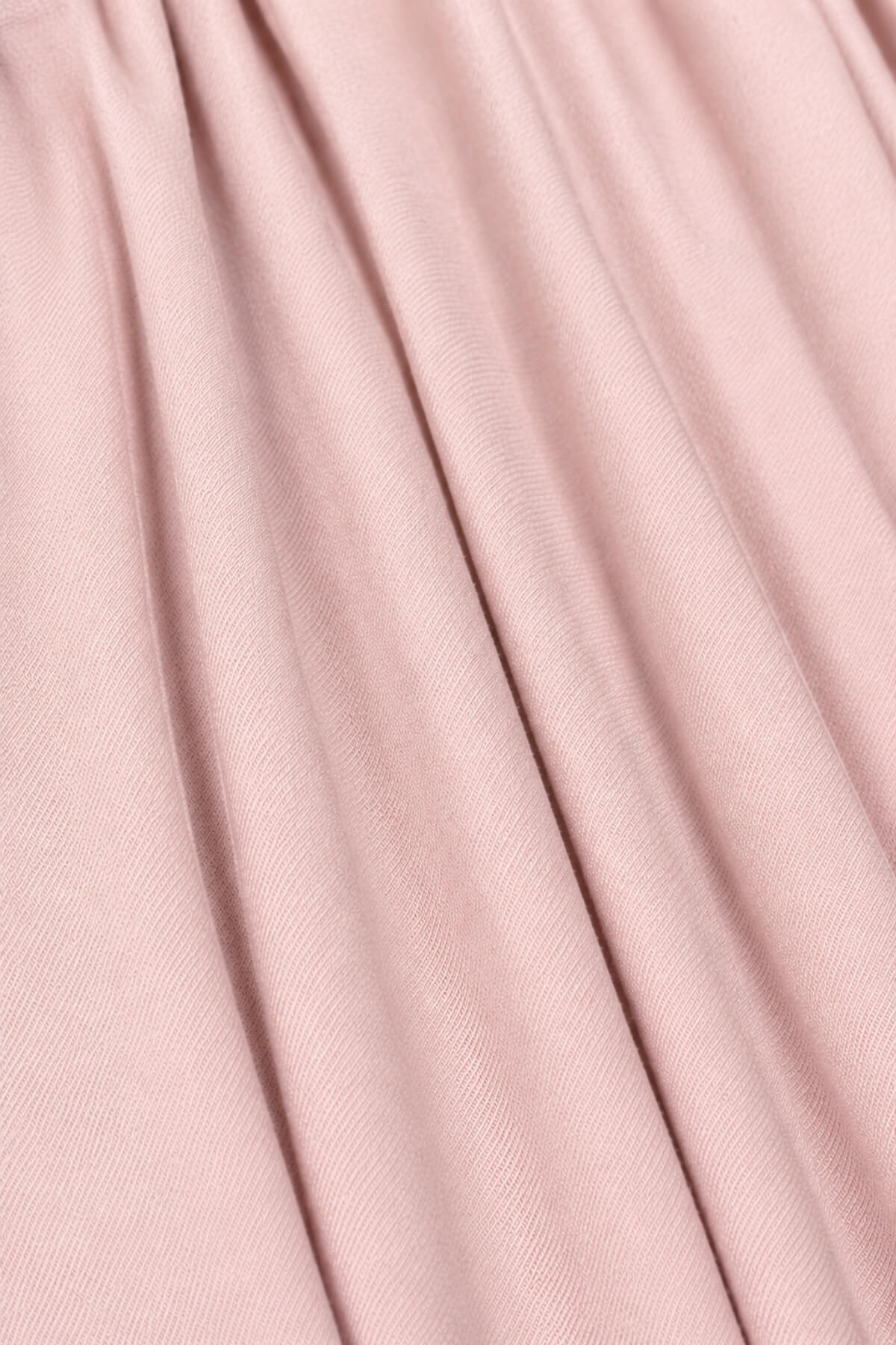 A close-up of draped dusty pink fabric with soft vertical folds and a fine woven texture.