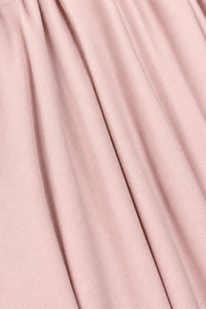 A close-up of draped dusty pink fabric with soft vertical folds and a fine woven texture.