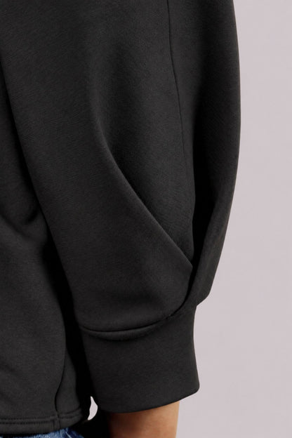 Close-up detail of a black long-sleeve sweatshirt sleeve with a ribbed cuff, worn by a model.