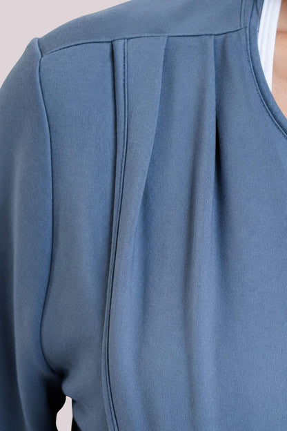 Close-up of a dusty blue long-sleeve top with a pleated front detail, worn by a model.