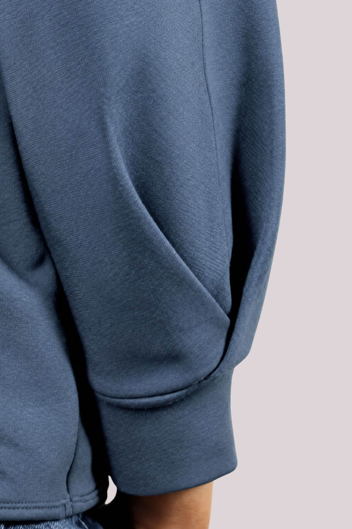 Close-up of a person wearing a slate blue sweatshirt, showing the sleeve and ribbed cuff against a light gray background.