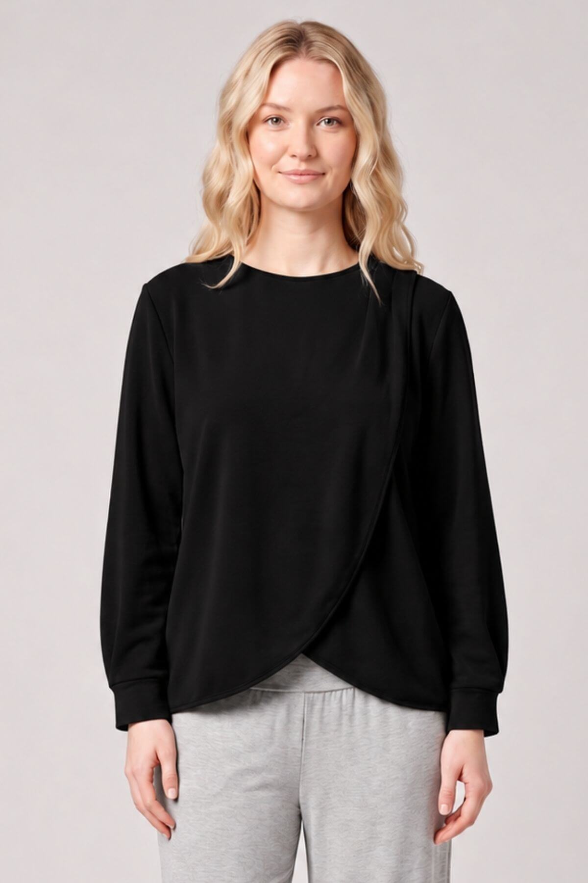 A woman modeling a black long-sleeve wrap-style top with a crew neck, paired with light gray sweatpants, against a solid light gray studio background.