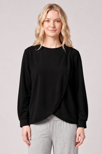 A woman modeling a black long-sleeve wrap-style top with a crew neck, paired with light gray sweatpants, against a solid light gray studio background.