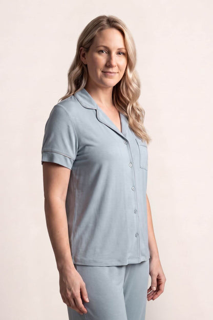 A woman modeling a light blue short-sleeve pajama top and matching pants against a plain beige studio background.