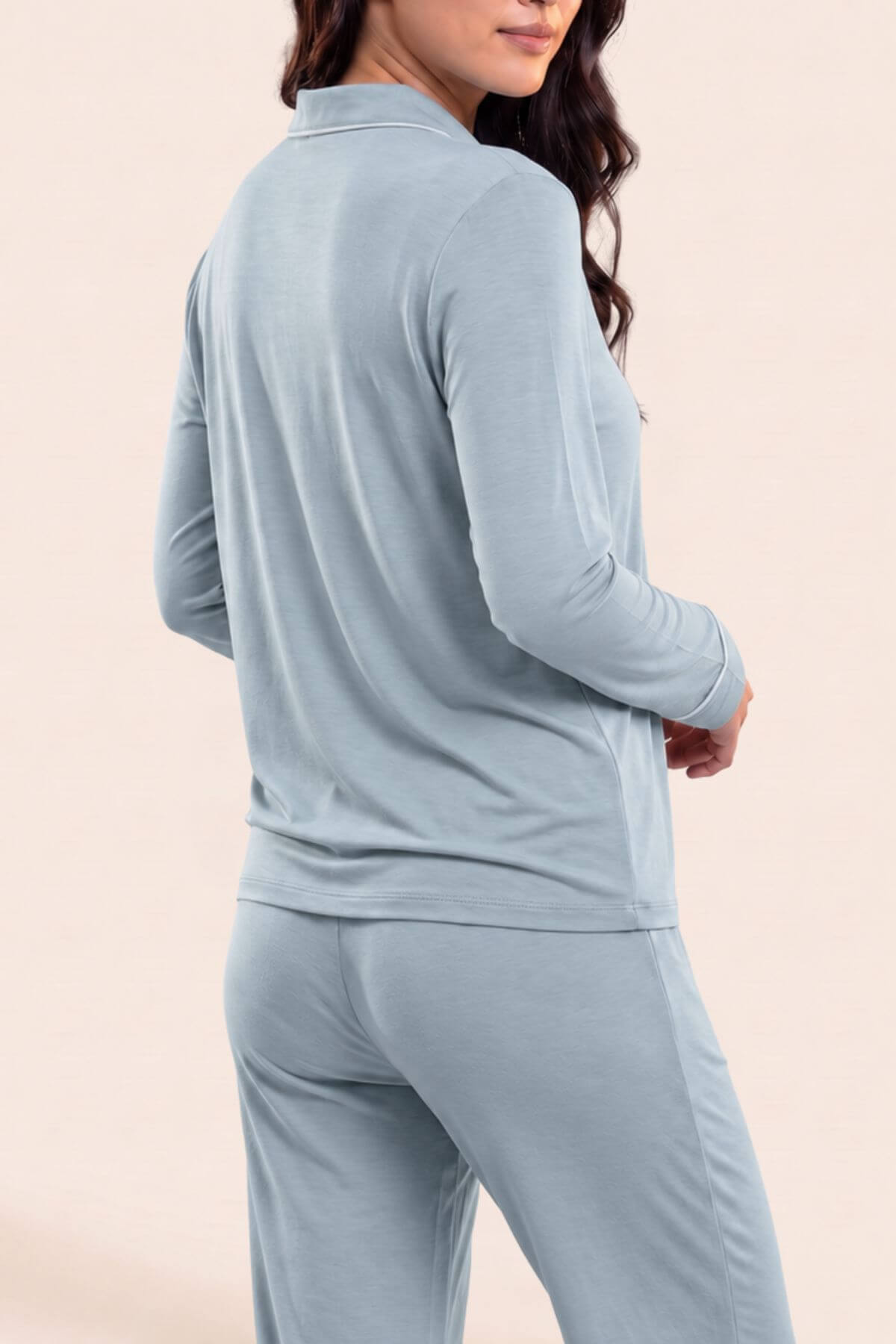 A woman wearing a light blue matching two-piece loungewear set, featuring a long-sleeve quarter-zip top and matching pants, shown from a three-quarters back view against a solid pale beige background.