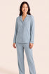 A woman modeling a light blue long-sleeve pajama set with a button-front shirt and matching pants against a solid pale beige background.