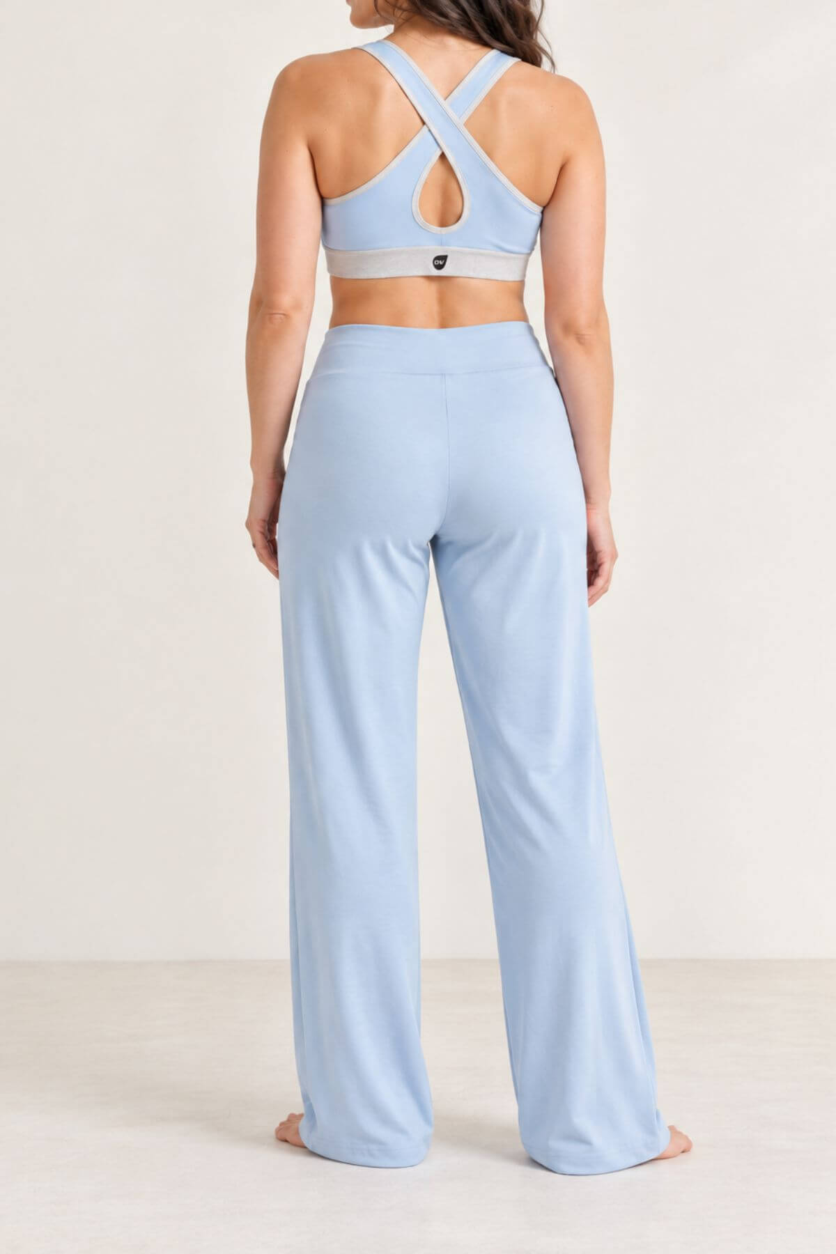 A woman shown from the back wearing a light blue activewear set consisting of a sports bra with crisscross straps and matching high-waisted wide-leg pants, against a plain off-white studio background.