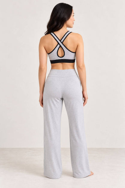 A woman shown from the back wearing a light gray and black sports bra and matching light gray wide-leg sweatpants in a studio setting.